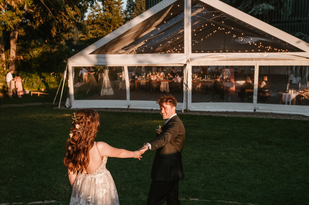 groom holding brides hand walking towards the reception and smiling 