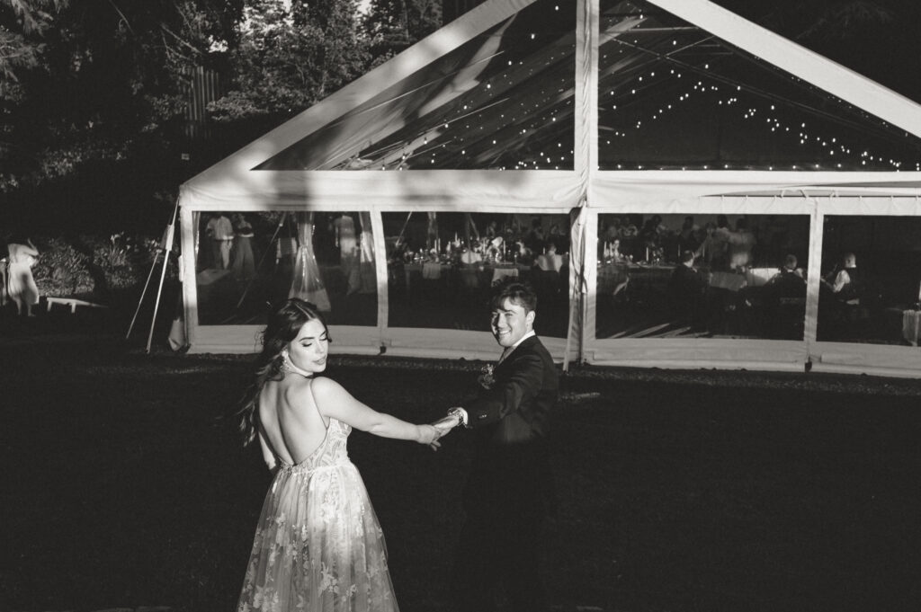 black and white of bride and groom leading each other towards reception tent 