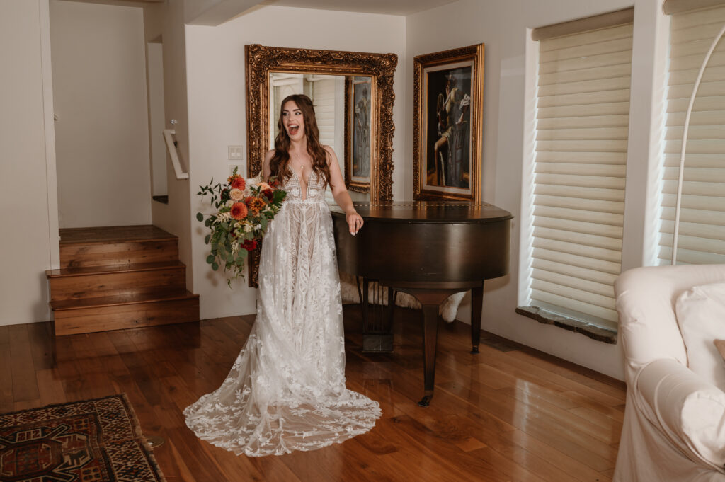 bride smiling and laughing while holding her bridal bouquet and leaning up against a piano 