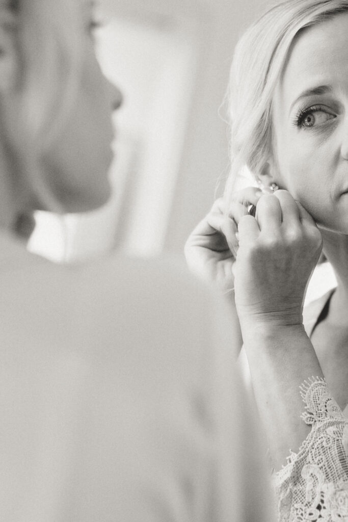 bride putting her own earring in while looking in the mirror 