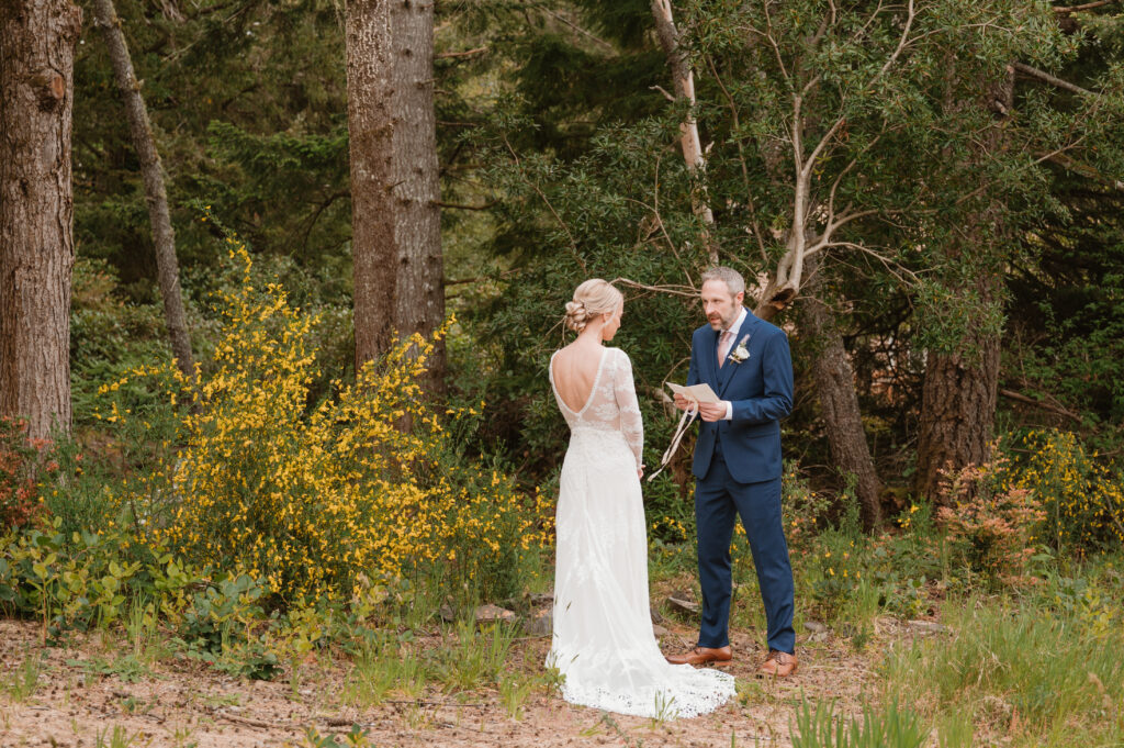 bride looking at groom as he reads her vows from his vow book 