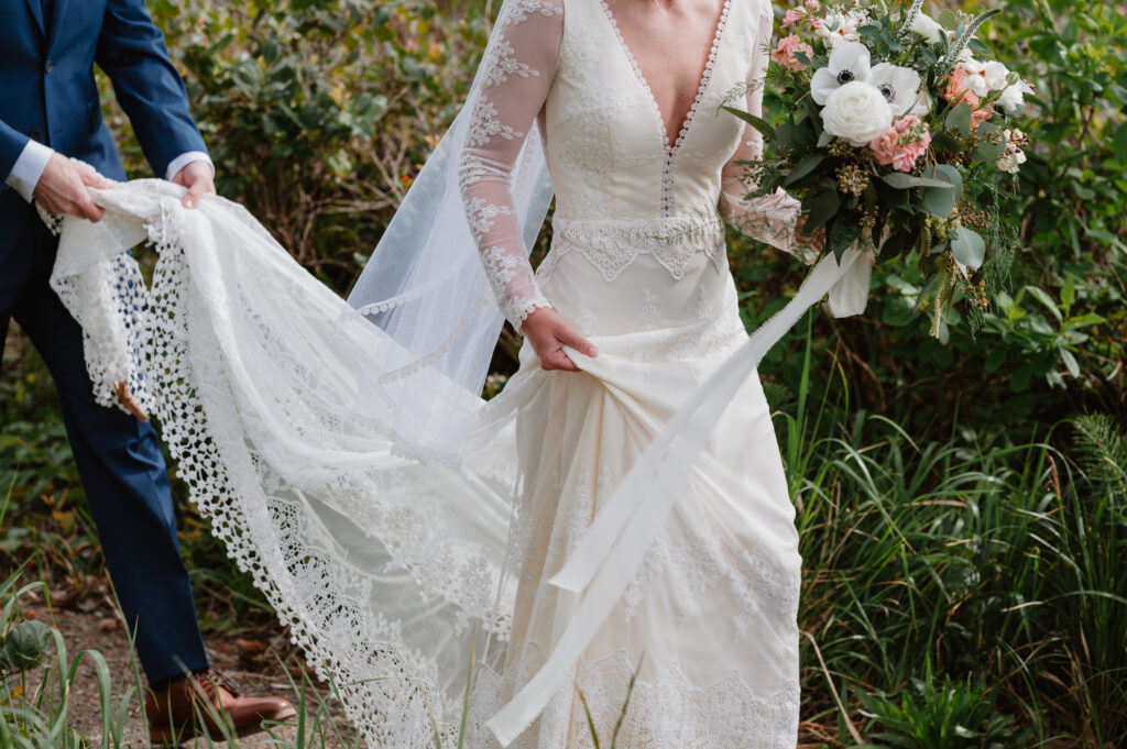 bride walking with her bouquet while the groom holds her train on the way to their intimate Oregon coast wedding ceremony 