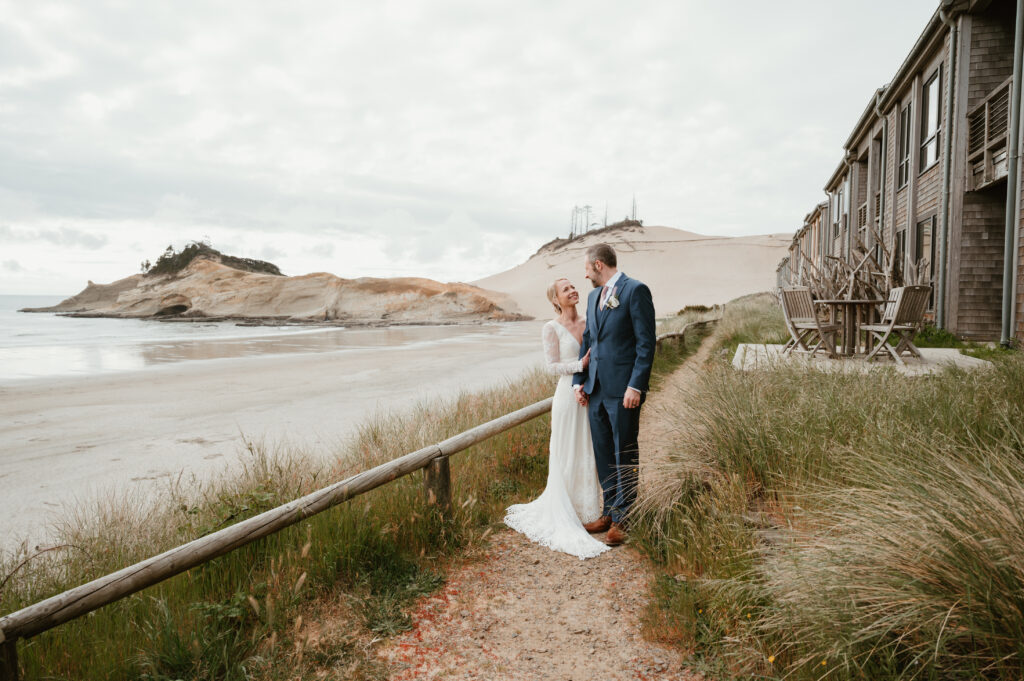 bride and groom holding hands and smiling at each other posed in front of a sand dune 